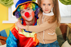 Little girl hugging a cheerful clown with rainbow coloured hair.